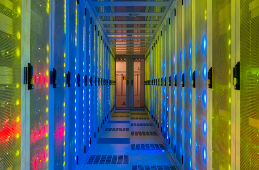 A brightly lit data center aisle with rows of server racks on both sides, illuminated by blue and yellow LED lights
